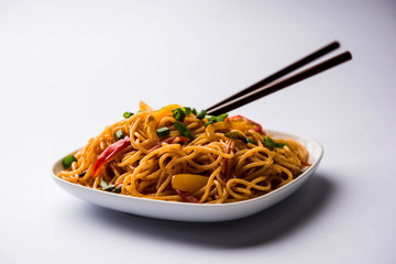 Schezwan Noodles or vegetable Hakka Noodles or chow mein is a popular Indo-Chinese recipes, served in a bowl or plate with wooden chopsticks. selective focus