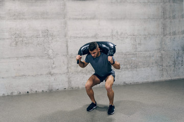 Strong Caucasian sporty man in sportswear lifting Bulgarian training bag. Don't stop until you are...