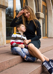 young stylish casual mother with her lovely child son are sitting in the park on stairs, looking each other and smiling happy. lifestyle concept