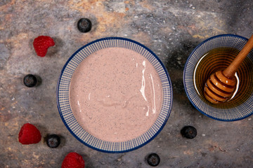 Plain acai bowl surrounded with raspberries, blueberries and honey 