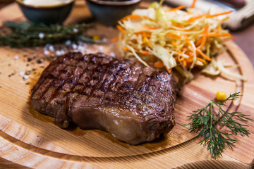 Big meat steak with vegetables, greenery and sauces on wooden table in luxury restaurant