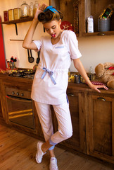  nurse with long legs and stylish hairstyle is looking down and showing tongue with  one hand near her head on the wooden kitchen background 