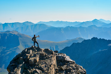 The man in the foreground stands on a cliff and enjoys the view of the sunrise in the mountains.