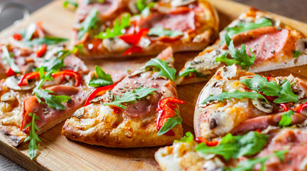 slices Pizza with Mozzarella cheese, mushrooms, ham, tomato sauce, salami, pepper, Spices and Fresh arugula. Italian pizza on wooden table background