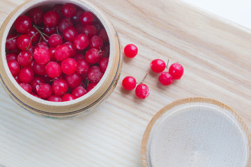 Wooden bowl with beautiful frozen cranberries and cap on wooden background. Soft focus. Top view. Health food concept.