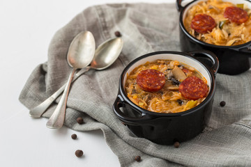 Slovak Christmas national cabbage soup in two small black pots with sausage on the tablecloth background.