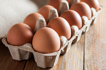 Large brown chicken eggs in green carton box on wooden table.