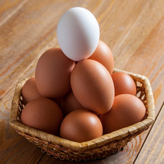 Group of chicken brown eggs and one white lie in a wicker basket on a wooden table. Cropped to...