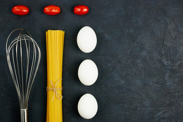 Top view of raw pasta next to egg and cherry, fresh tomatoes, on black background. copy space.
