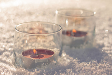 Two candles in the glasses on the snow.