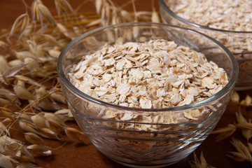 Oat ears stems and oat flakes in a bowl on a dark brown wood background. oat flakes big and small size grind. oatmeal flakes coarse. large-sized flakes. Useful fiber-rich product. close up