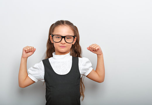 Fun happy girl in eyeglasses showing her muscle arms in school uniform clothing on blue background with empty copy space. Healthy concept