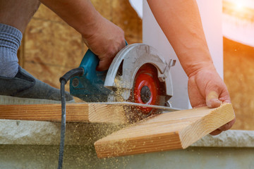 Building contractor worker using hand held worm drive circular saw to cut boards on a new home...