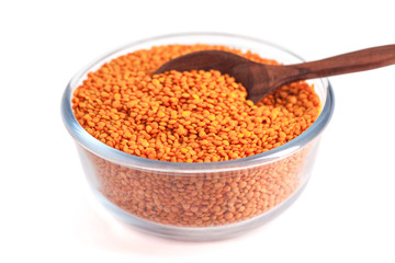 Red lentil in glass bowl with wooden spoon isolated on white background