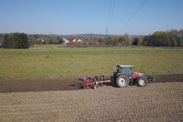 Fototapeta premium A farmer on a red tractor with a seeder sows grain in plowed land in a private field in the village area. Mechanization of spring field work. Farmer's everyday life. Processing of land. The agrarian.