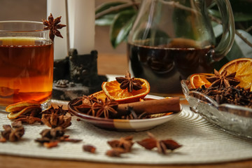 Beautiful composition with anise, cloves, cinnamon stick and powder, tea and dried orange. Wooden table, rustic background and candle light. Close-up.