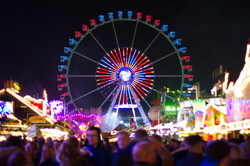 ferris wheel at night with blurry crowd in the foreground - obrazy, fototapety, plakaty