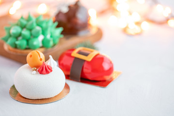 Mini mousse pastry desserts covered with velour or glaze. Garland lamps bokeh on background. Modern european cake. French cuisine. Christmas theme.