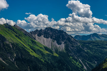 Felswände und grüne Flächen und Berggipfel mit blauem Himmel und einigen Wolken