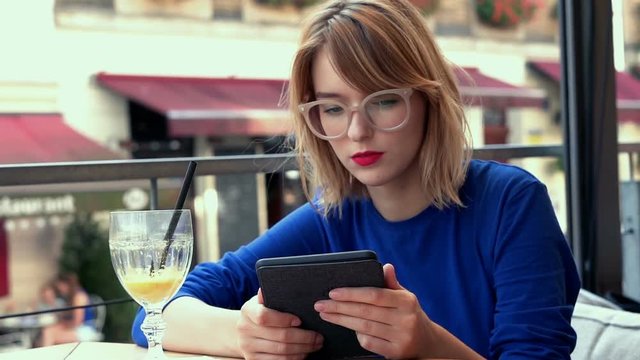 Young woman reading something on e-book sitting in cafe
