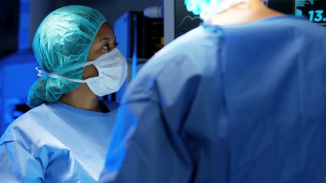 Laparoscopic surgical operation transmitted on hospital monitors being performed by multi ethnic female training as surgeon wearing surgical gloves and scrubs 
