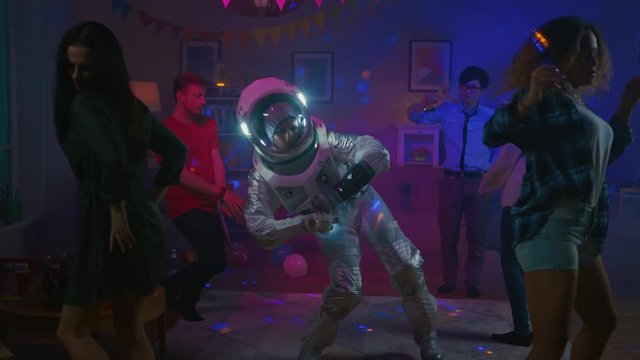 At the College House Costume Party: Fun Guy Wearing Space Suit Dances Off, Doing Groovy Funky Robot Dance Modern Moves. With Him Beautiful Girls and Boys Dancing in Neon Lights. In Slow Motion.