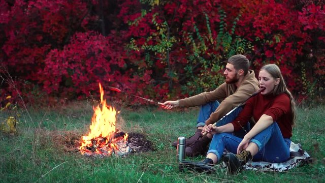 ood friends sitting on the ground frying food on outdoor picnic barbecue in colorful red autumn forest in slow motion