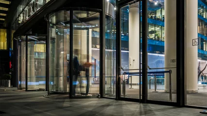 Photo sur Plexiglas construction de la ville le flux de personnes passant par la porte tournante de l& 39 immeuble de bureaux moderne à la fin de la journée de travail