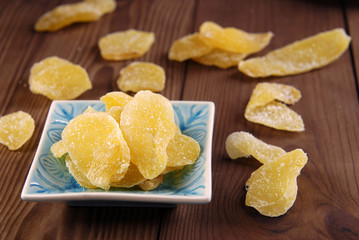 Pieces of dry ginger in sugar on a plate on a brown wooden background.