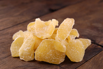 Pieces of dry ginger in sugar on a plate on a brown wooden background.