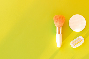 Brush for applying blush and cotton sponge discs with removable razor cartridge on a light green background in the sun with space for text. Creative idea for beauty products and make-up. Flat lay.