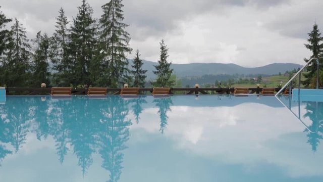 swimming pool with calm blue water in mountain hotel. mountains, cloudy sky and pines are reflecting in the water