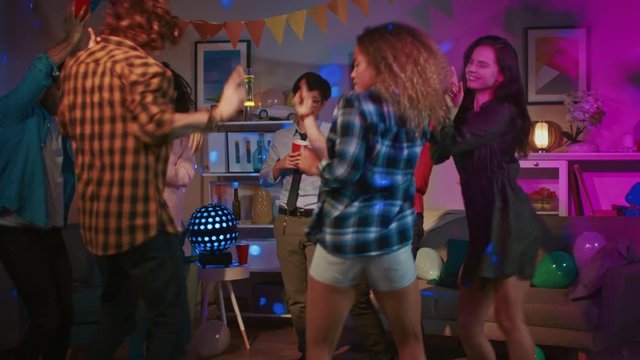 At the College House Party: Diverse Group of Friends Have Fun, Dancing and Socializing. Boys and Girls Dance in thr Circle. Girl Takes Glass with Drink from the Tray and Joins the Group.
