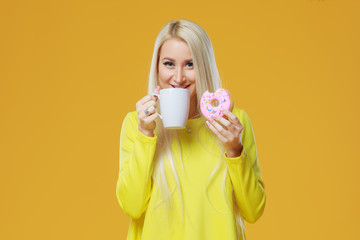 Young blond woman eating a delicious donut with closed eyes for pleasure. licking fingers with cream. Cup of coffee. Concept of food and Tasty