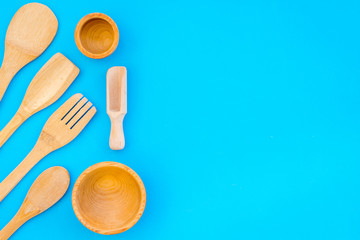 Fototapeta na wymiar woodenware set with spoon, fork and bowl on blue backgtound top view space for text