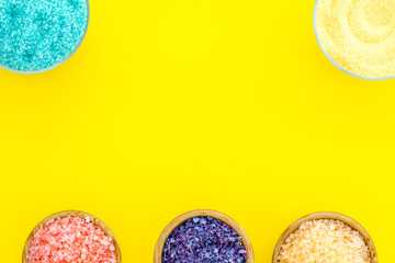 Spa salt background. Colorful spa salt in bowls on yellow background top view. Yellow, turquoise, pink, purple spa salt copy space