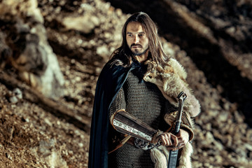 Naklejka premium Long haired knight with the two-handed sword. Rocks on the background.