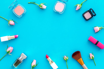 Rose, pink decorative cosmetics frame. Lipstick, bulk, eyeshadow and small rose flowers on blue background top view copy space