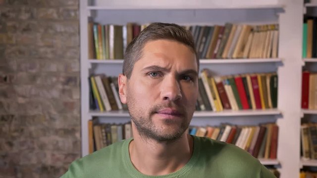 Adult man listens and gets surprised. Bookshelves on the background