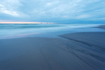 landscape at dusk, sandy beach and a smooth sea surface during the 
