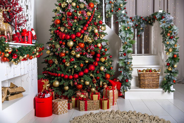 White room interior in red tones with New Year tree decorated, present boxes and artificial fireplace