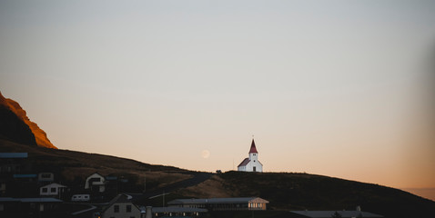 Fototapeta na wymiar Church on top of a hill and under a mountain, with the moon in the background.
