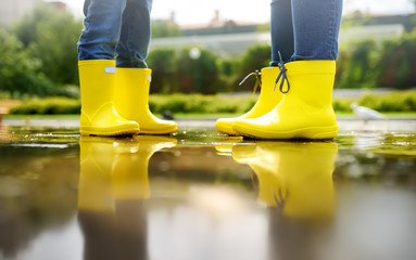 Mother and child in yellow boots playing in a puddle on a summer day.