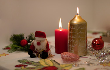 Candles lit with Christmas decoration and a Santa Claus doll on a tablecloth
