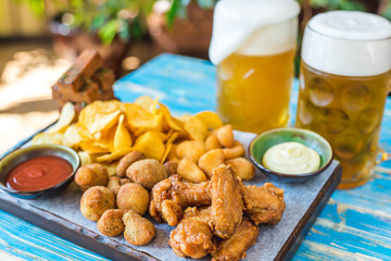 beer in glasses with snacks, chicken nuggets, chips and sauces