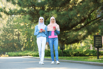 Muslim women with cups of coffee walking in park