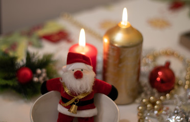 Santa Claus doll inside a bowl with on a Christmas tablecloth with candles