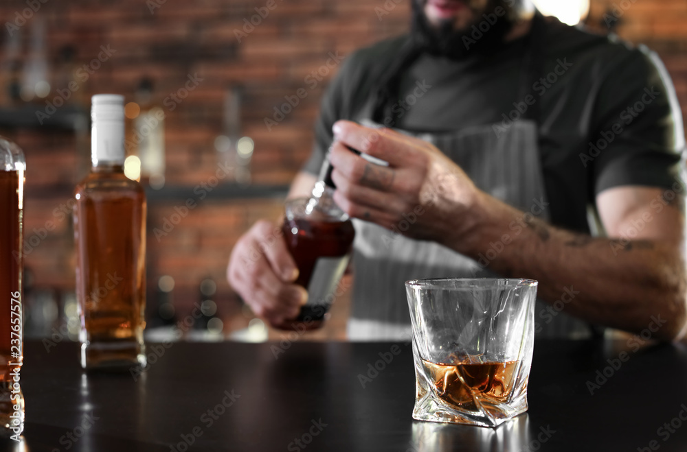 Poster Bartender at counter with bottles and glass of whiskey in bar, closeup. Space for text