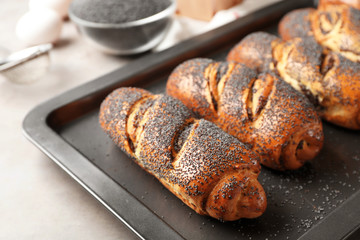 Baking tray with tasty poppy seed rolls  on table