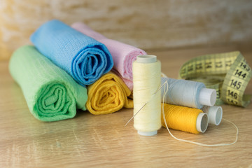 Rolls of colored fabric with a spool of thread and a needle on a wooden table. Raw material for...